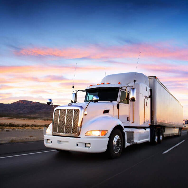 A semi-truck travelling through the desert at sunset